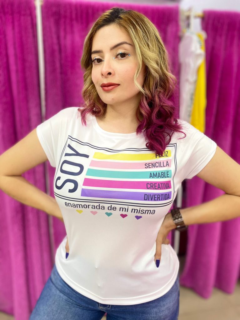 Mujer usando camiseta blanca con frases de autoestima en colores vibrantes y la leyenda “Soy enamorada de mí misma”