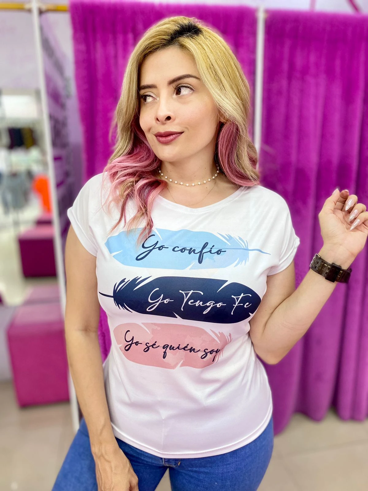 Mujer usando camiseta blanca con diseño de tres plumas de colores y frases inspiradoras: “Yo confío”, “Yo tengo fe”, “Yo sé quién soy”.